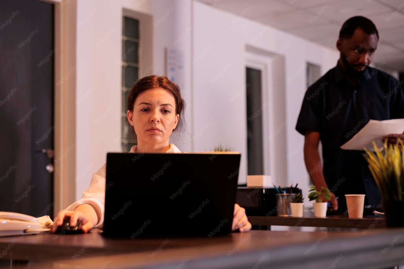 An office professional reviews information on a laptop at a desk in a shared workplace.